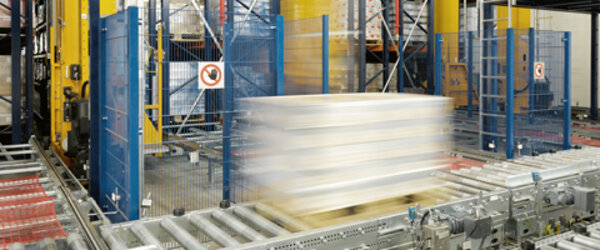 Eine bepackte Palette wurde gerade aus dem Hochregallager ausgelagert und fährt auf der Fördertechnik zur Auslagerungsstelle