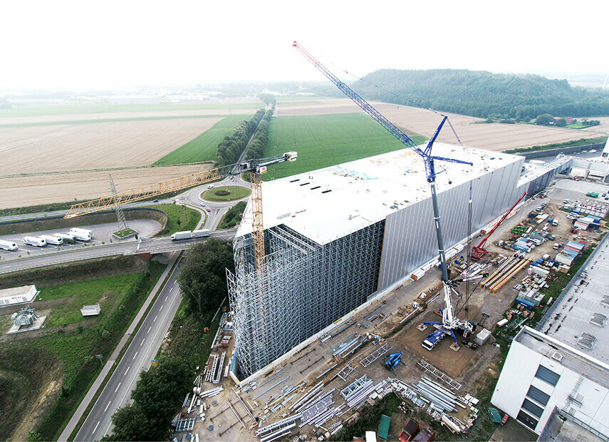 Eine Luftaufnahme einer Großbaustelle mit einem hohen Kran neben einem teilweise fertiggestellten Gebäude.