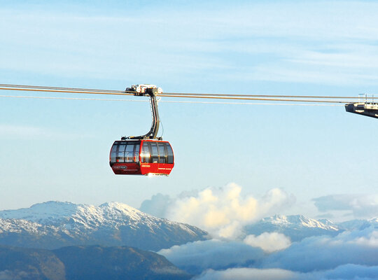 Eine atemberaubende Aufnahme einer roten Gondel, die über den Bergen und Wolken schwebt Eine atemberaubende Aufnahme einer roten Gondel, die über den Bergen und Wolken schwebt