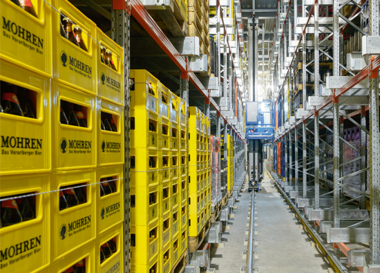 Stacker crane moves through rack aisle and picks up pallets full of beer crates